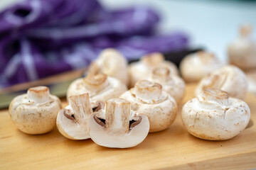 Shallow depth-of-field close-up of whole and halved button mushrooms on a wooden board. Focus on foreground detail, texture, and preparation for cooking concepts.
