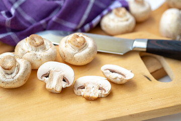 Shallow depth-of-field close-up of whole and halved button mushrooms on a wooden board. Focus on foreground detail, texture, and preparation for cooking concepts.