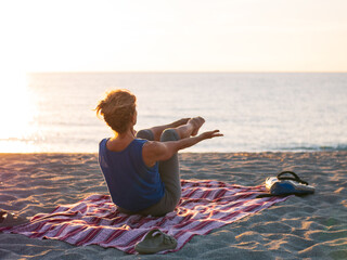 Woman practicing yoga on a quiet sandy beach at sunrise in Calabria, Italy, with warm golden light over the calm sea and long shadows stretching across the sand