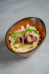 A vibrant bowl of octopus pasta with herbs and rich sauce entices food lovers