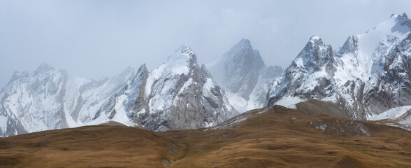 Snow-capped mountains rising above a remote high-altitude valley in Naryn province, Kyrgyzstan, under soft misty light.