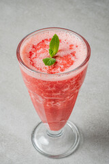 A vibrant pink smoothie sits in a tall glass, topped with fresh mint, perfect for hot days
