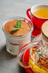 Tiramisu in a glass next to fragrant herbal tea in a warm, inviting atmosphere