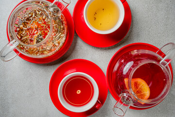 Herbal and citrus teas elegantly presented in bright red vessels on a grey surface