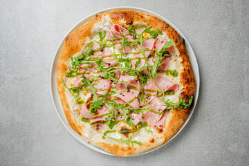 A fresh pizza topped with ham, arugula, and pesto is ready to be enjoyed