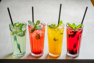 Four vibrant drinks sit on a sleek table, each enhanced by fresh mint and ice, inviting relaxation