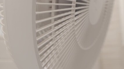 A white plastic electric fan is operating with its blades spinning rapidly behind the protective grille. The moving blades generate a steady, whooshing sound of airflow.