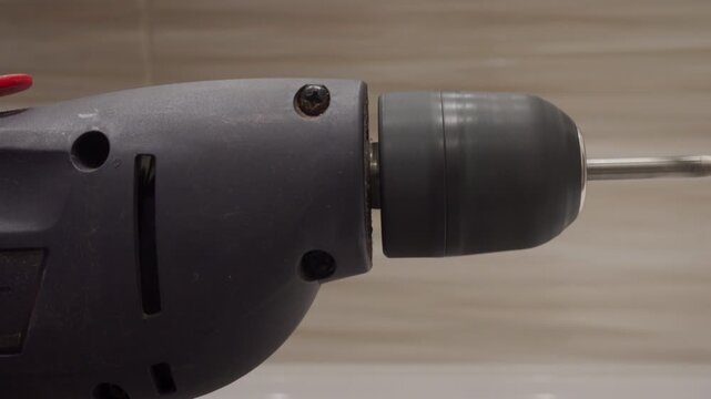 A plastic electric power drill with a metal bit attached is turned on and runs at a fast speed. The rapid rotation produces a loud, high-pitched motor whirring and whining sound.