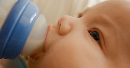 Close up of a newborn child eating from a bottle lying on bed. Mother feeds the baby using powdered milk.