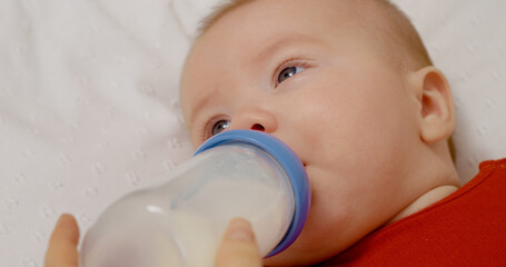 Mother's hands feeding her newborn by bottle. Baby care of a loving mother at home. Childcare concept.