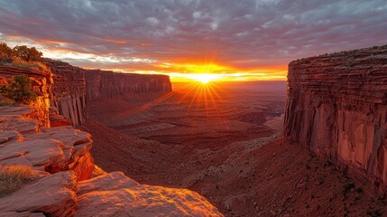 Sunrise bursts over canyon, red rock formations; dramatic sky, warm light, scenic