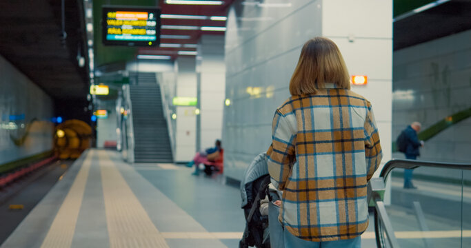 Female waiting patiently on subway platform, holding baby stroller while anticipating train arrival in urban transit environment - Powered by Adobe