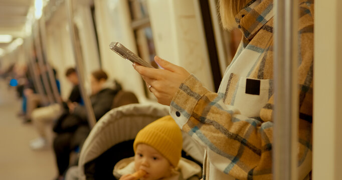 Young mother using her smartphone while commuting on a subway train with her baby in a stroller