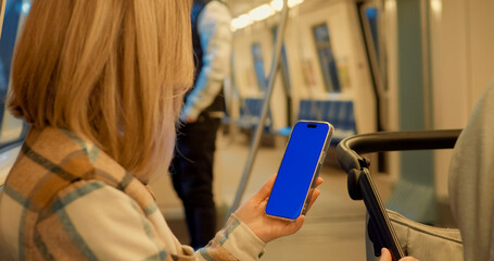 Urban commuter holding blue screen smartphone while seated inside subway train, showcasing digital communication in modern public transport environment. Chroma Key, Mockup Blue Screen on Subway