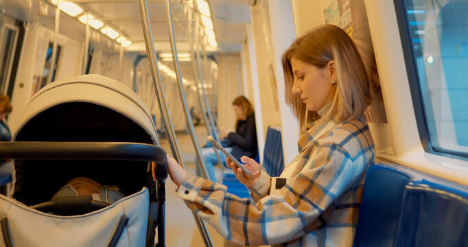 Subway car interior with young mother using her smartphone while traveling with a baby stroller - Powered by Adobe