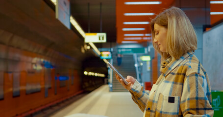 Subway platform scene with a young mother using her smartphone while waiting for the train