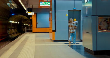 Young mother gently holding infant while walking across subway platform, moving toward elevator in urban transit setting © RecCameraStock