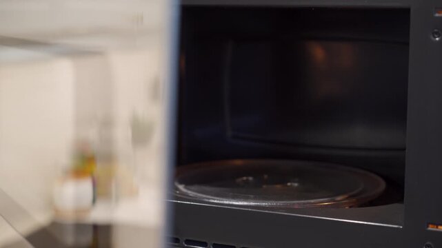 The glass door of microwave oven, revealing the empty interior and glass turntable, is opened with a sudden, mechanical click. internal venting fan runs, producing a low, consistent humming sound.