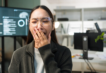 Tired woman programmer or IT specialist software developer yawning overtime working late at night failure debugging code on monitor computer screen.