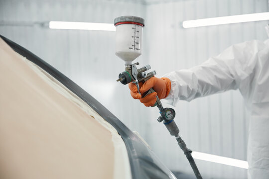 A technician carefully spraying high-quality automotive paint on a car door in a white garage