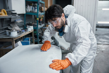 An auto body technician is sanding a car panel in a protective suit inside a workshop