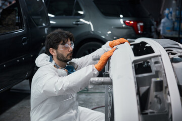 An automotive technician is repairing a car bumper in a workshop while wearing safety gear