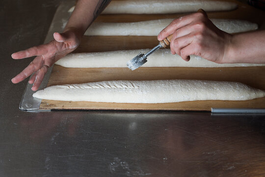 close up of a hand holding a knife for scoring baguette,  