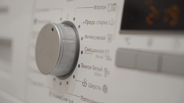 The plastic and metal control panel of a washing machine features a large program selector dial set to a delicate or wool wash program. The machine is running a slow drum rotation