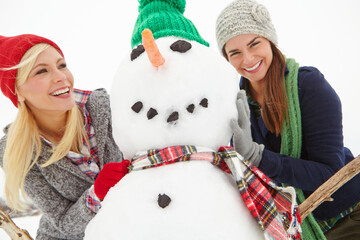 Women, friends and snowman on vacation, laugh or bonding for fun, games or excited in winter....