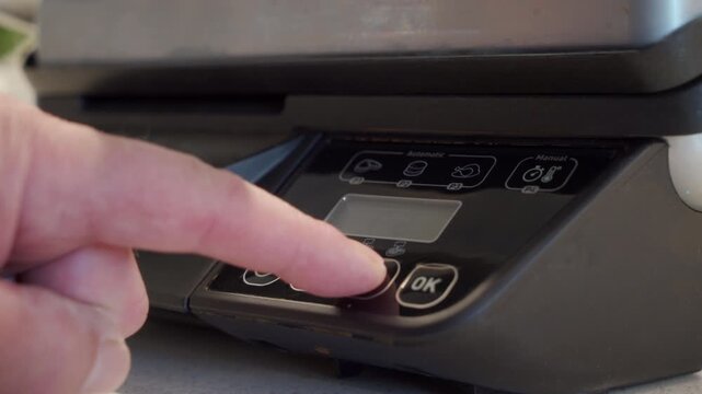 Plastic control panel of a black electric grill is touched by a finger to select an automatic cooking mode. The button press action is immediately followed by a short electronic beep sound.
