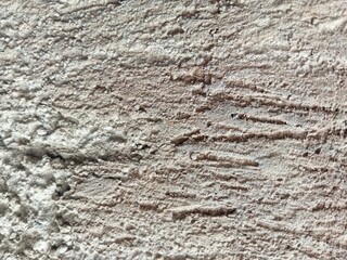 Close-up photo of a rough textured cement wall showing natural lines, scratches, and surface imperfections. The image highlights raw cement texture with detailed patterns and shadows, suitable for b