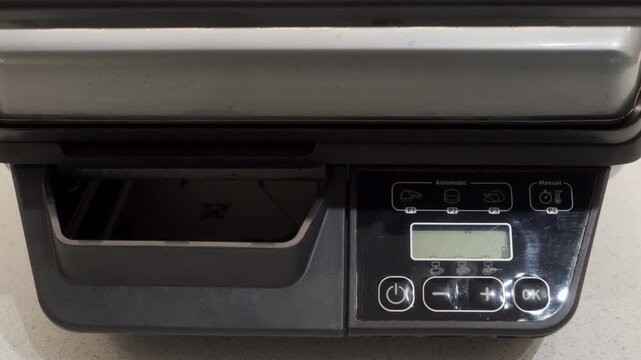 A plastic and metal electric grill completes its heating cycle and is ready for use. A short, electronic alert tone is emitted to indicate the cooking plates are fully preheated.