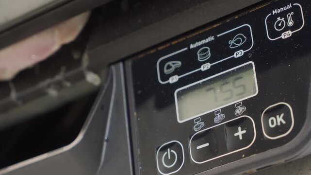 Chicken is being compressed and cooked between the metal plates of an electric grill, with the digital display showing a countdown time. The cooking action generates moderate sizzling sound.