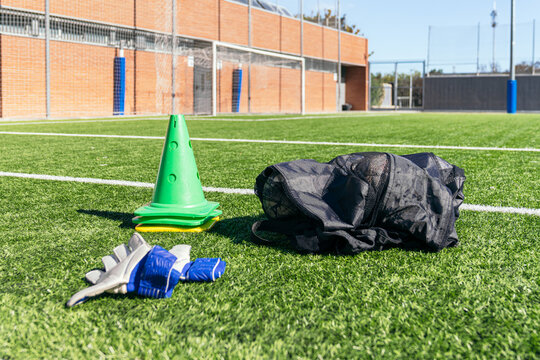 Football soccer training gear showing cones, goalie gloves, and a net bag on a green artificial turf field - Powered by Adobe