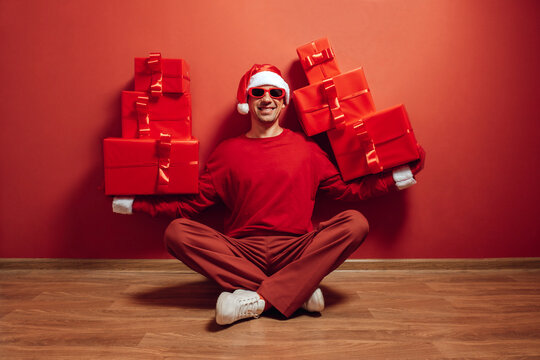 Person in Santa hat and red outfit balancing Christmas gifts indoors