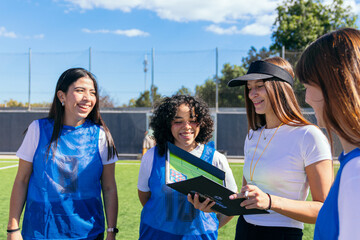 Coach reviewing game tactics on a clipboard with young female soccer players during outdoor training session © Koldo_Studio