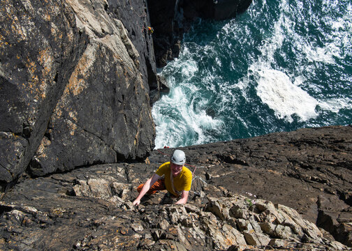 Climber with helmet scaling sea cliff at Gurnard's Head Cornwall