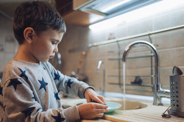 Child washing dishes in kitchen helping with housework