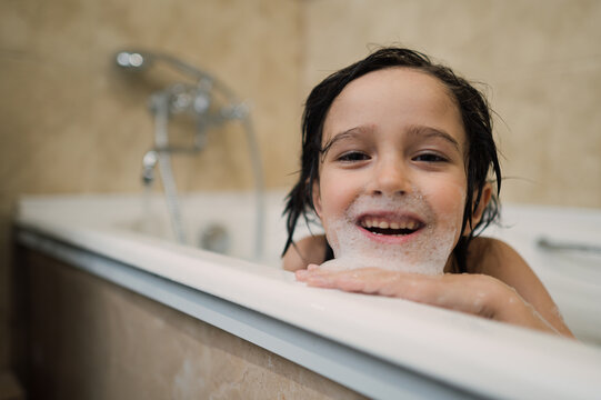 Smiling child with foam on face in bathtub enjoying bath time