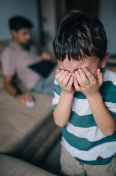 Crying child with father working remotely at home in living room