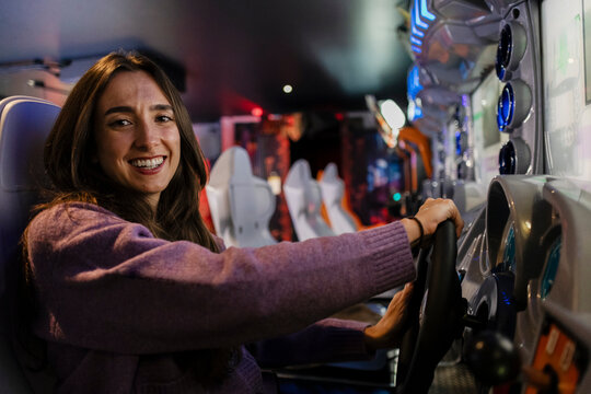 Smiling woman enjoying arcade racing video game indoors
