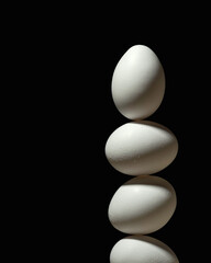 Three white eggs stacked in tall column on black background forming dramatic minimalist scene with strong contrast and fragile balance