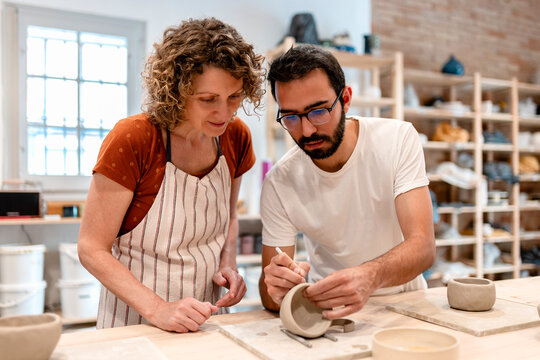 Teacher guiding student in ceramic art pottery class at workshop