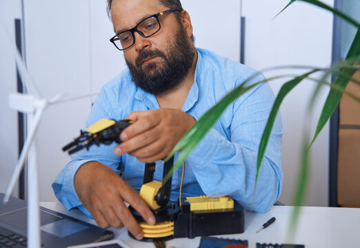 Engineer working on robotic arm in office laboratory with wind turbine