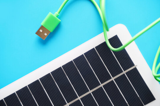 Green USB cable with solar panel on blue background for renewable energy