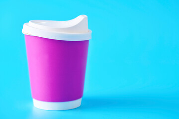 Pink coffee cup with lid in studio shot on blue background