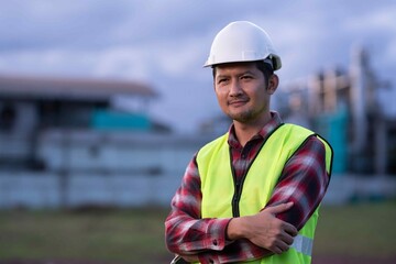 Male engineer crossing arms with a calm smile at factory site, representing leadership, workplace safety, and industrial reliability.