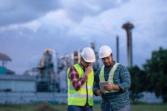 Two engineers discussing industrial project data on tablet, reflecting teamwork, communication, and collaboration in factory operations.