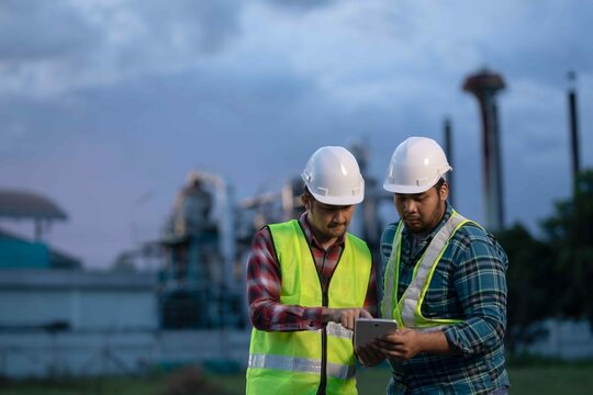 Industrial engineers using tablet to check blueprints and coordinate tasks, showing focus, precision, and collaboration in field operations. - Powered by Adobe