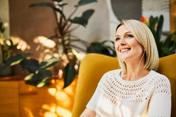 Smiling woman with earphones relaxing in sunny home interior